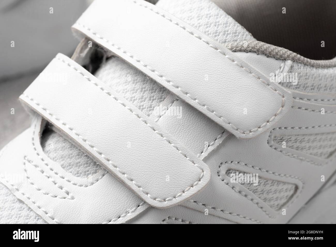 Photo des sneakers blanches pour enfant. Macro photographie de baskets de sport en cuir et tissu avec fermeture Velcro, vue du dessus, monochrome Banque D'Images
