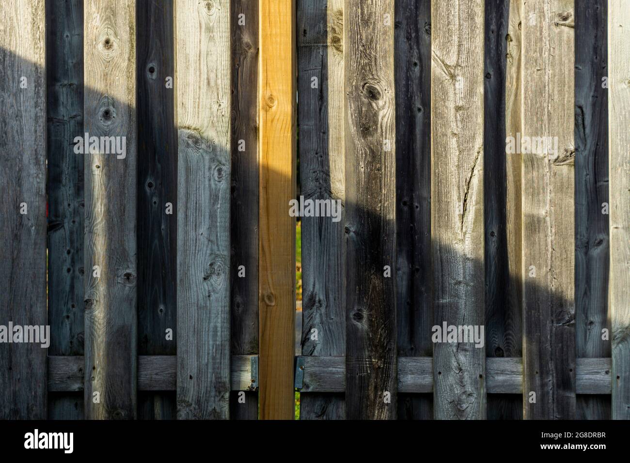 Jeu diagonal de lumière et d'ombre sur une ancienne clôture en bois patiné soutenue par une batte relativement nouvelle. Banque D'Images