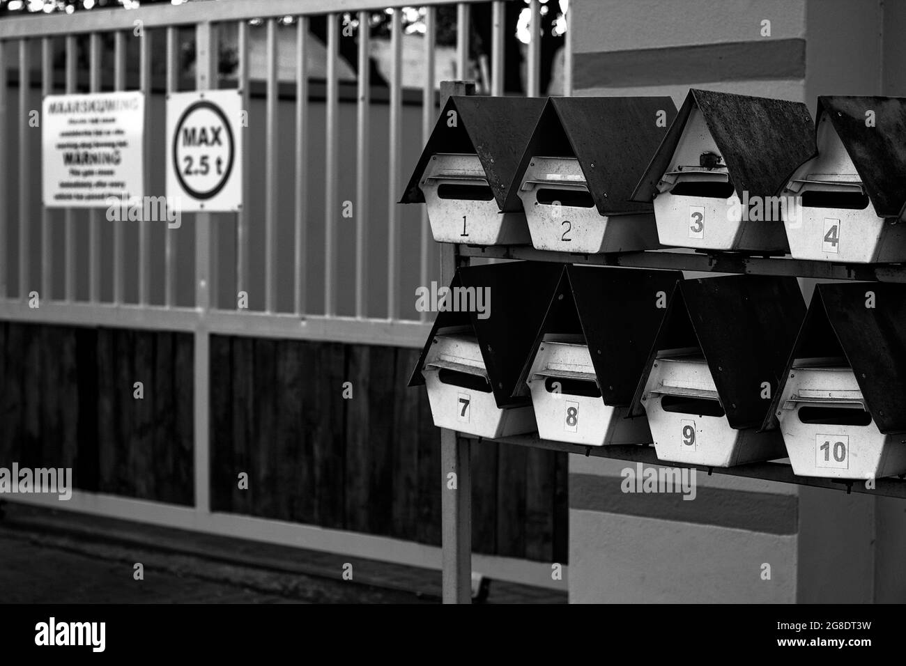 Prise de vue en niveaux de gris de petites boîtes aux lettres en forme de maison près de la clôture métallique Banque D'Images