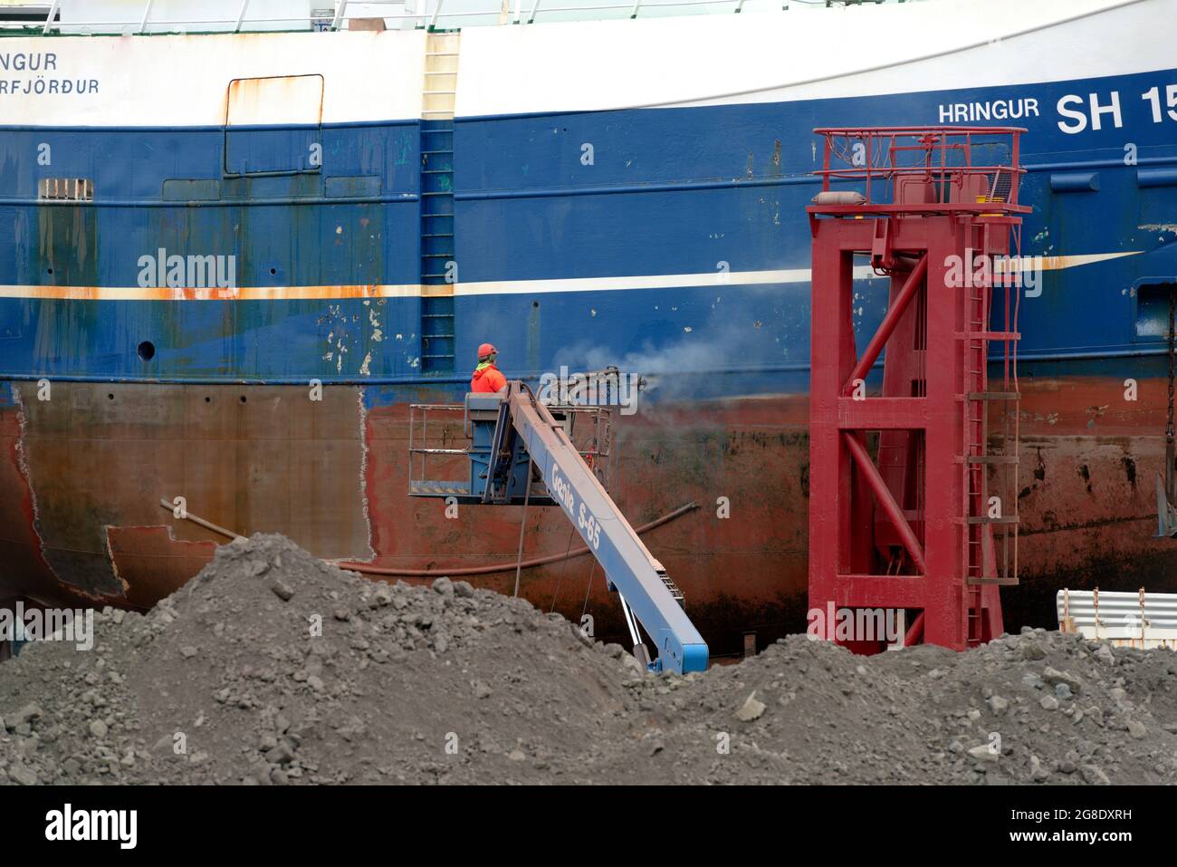 Un homme retire la peinture d'un bateau dans un quai sec prêt à repeindre. Vieux port, Reykjavik, Islande. Banque D'Images