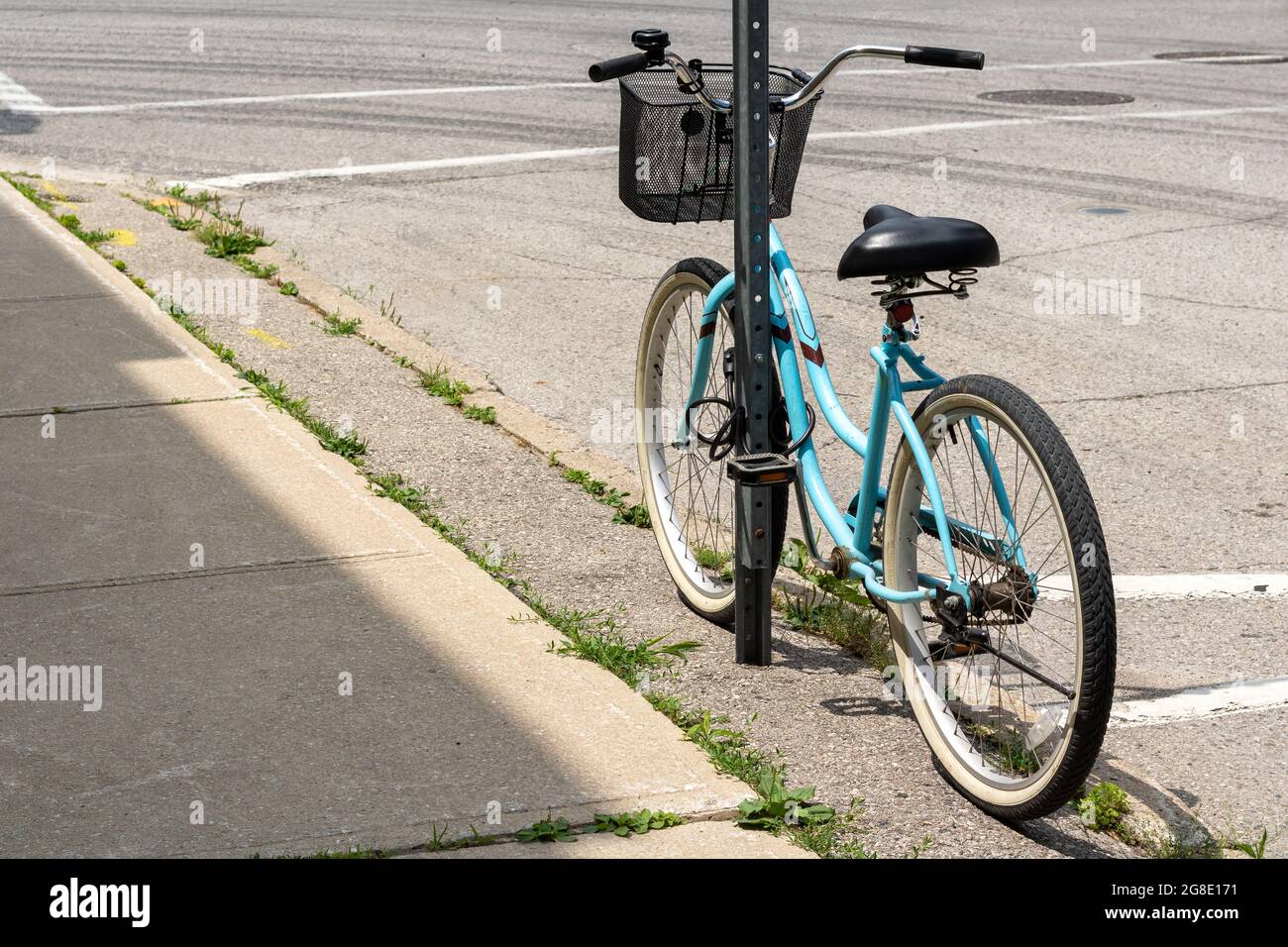 Vélo de croisière bleu avec panier noir incliné contre et verrouillé à un poteau de signalisation routière. Banque D'Images