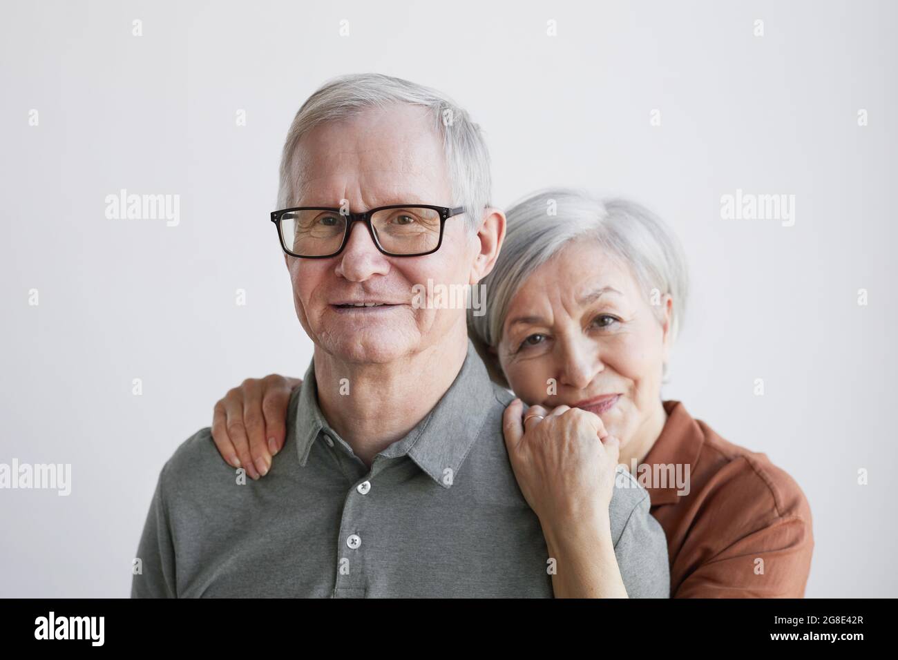 Portrait minimal d'un couple de personnes âgées aimant qui s'embrasse et regarde l'appareil photo tout en se tenant sur un fond blanc Banque D'Images