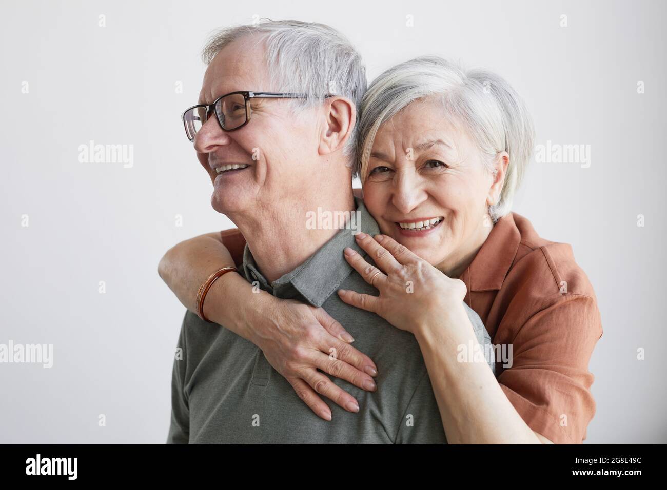 Portrait minimal d'un couple senior insouciant qui s'embrasse et regarde l'appareil photo tout en se tenant sur un arrière-plan blanc Banque D'Images