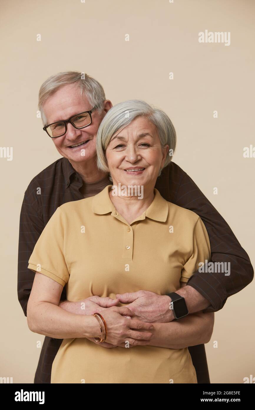 Portrait de couple senior à la taille minimale tenant et regardant l'appareil photo tout en se tenant contre un arrière-plan beige Banque D'Images