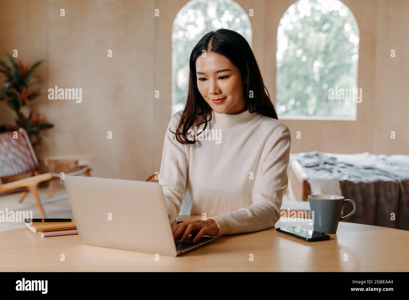 Une jeune femme asiatique adolescente porte un chandail avec le sourire  dans le salon. Bonne et réussie fille utilisant l'ordinateur portable avec  Notebook.concept de technologie en ligne. Mode de vie portrait d'hiver.