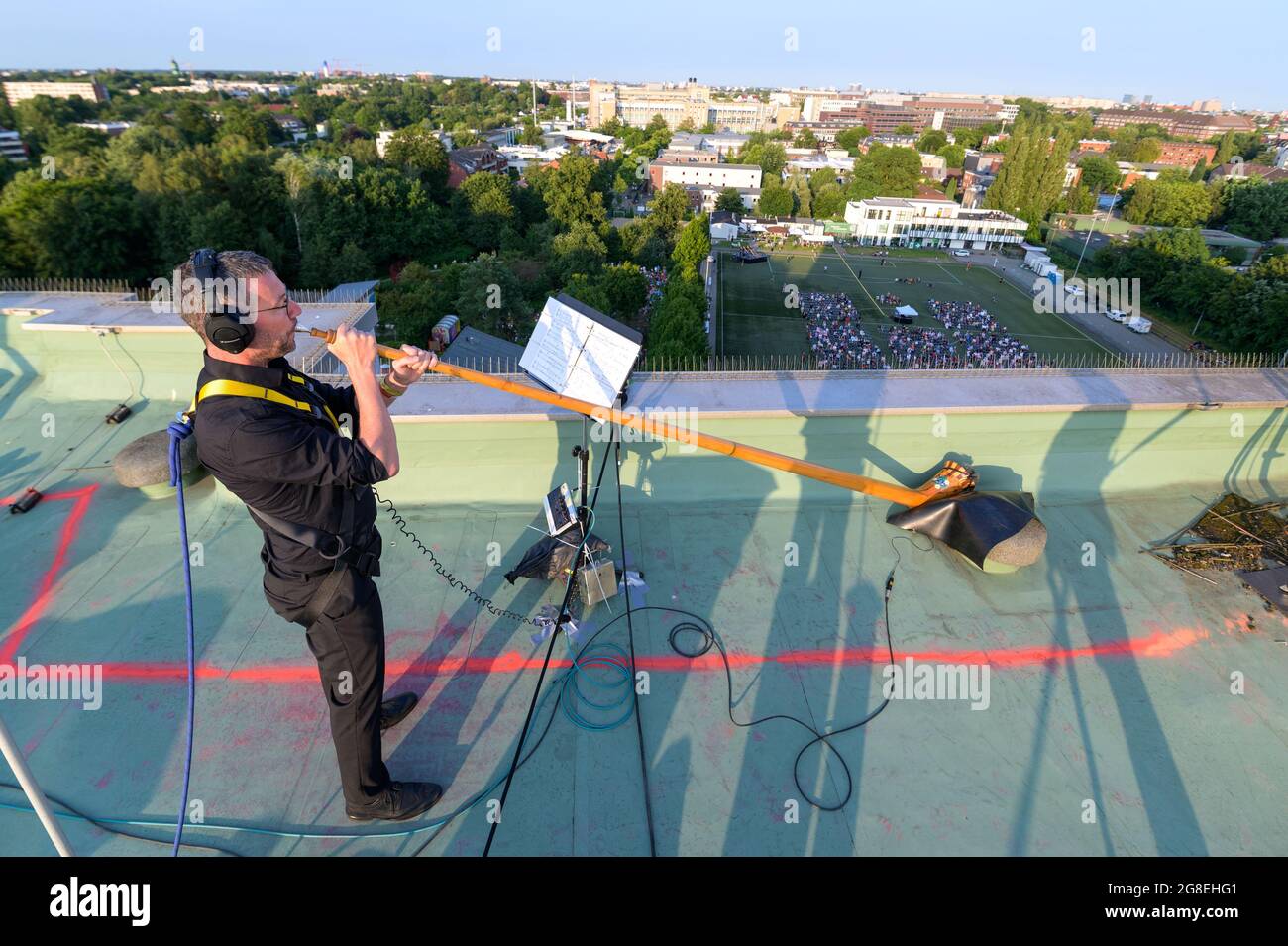 Hambourg, Allemagne. 17 juillet 2021. Un musicien souffle son Alphorn sur le toit d'une tour alors que des centaines de spectateurs écoutent sur un terrain de football et partout. En coopération avec Kampnagel et Elbphilharmonie, l'Orchestre symphonique de Dresde joue sur les toits du Lenzsiedlung et du SV Grün-Weiß Eimsbüttel. 500 spectateurs inscrits pouvaient s'asseoir dans le stade. Credit: Jonas Walzberg/dpa/Alay Live News Banque D'Images