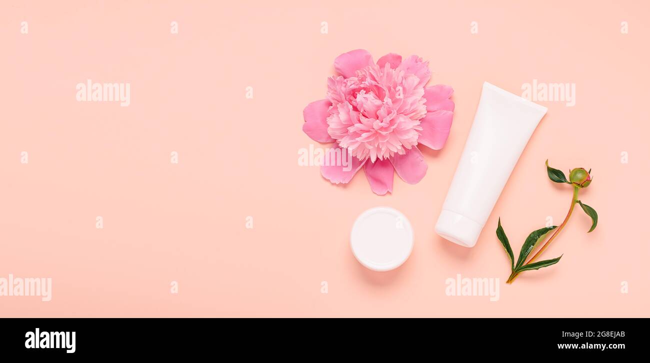 Produits cosmétiques crème gel shampooing baume dans différentes bouteilles sur fond rose avec fleurs fraîches pivoines Banque D'Images
