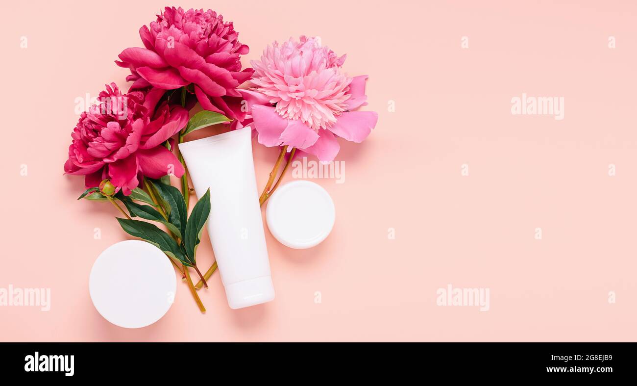 Produits cosmétiques crème gel shampooing baume dans différentes bouteilles sur fond rose avec fleurs fraîches pivoines Banque D'Images
