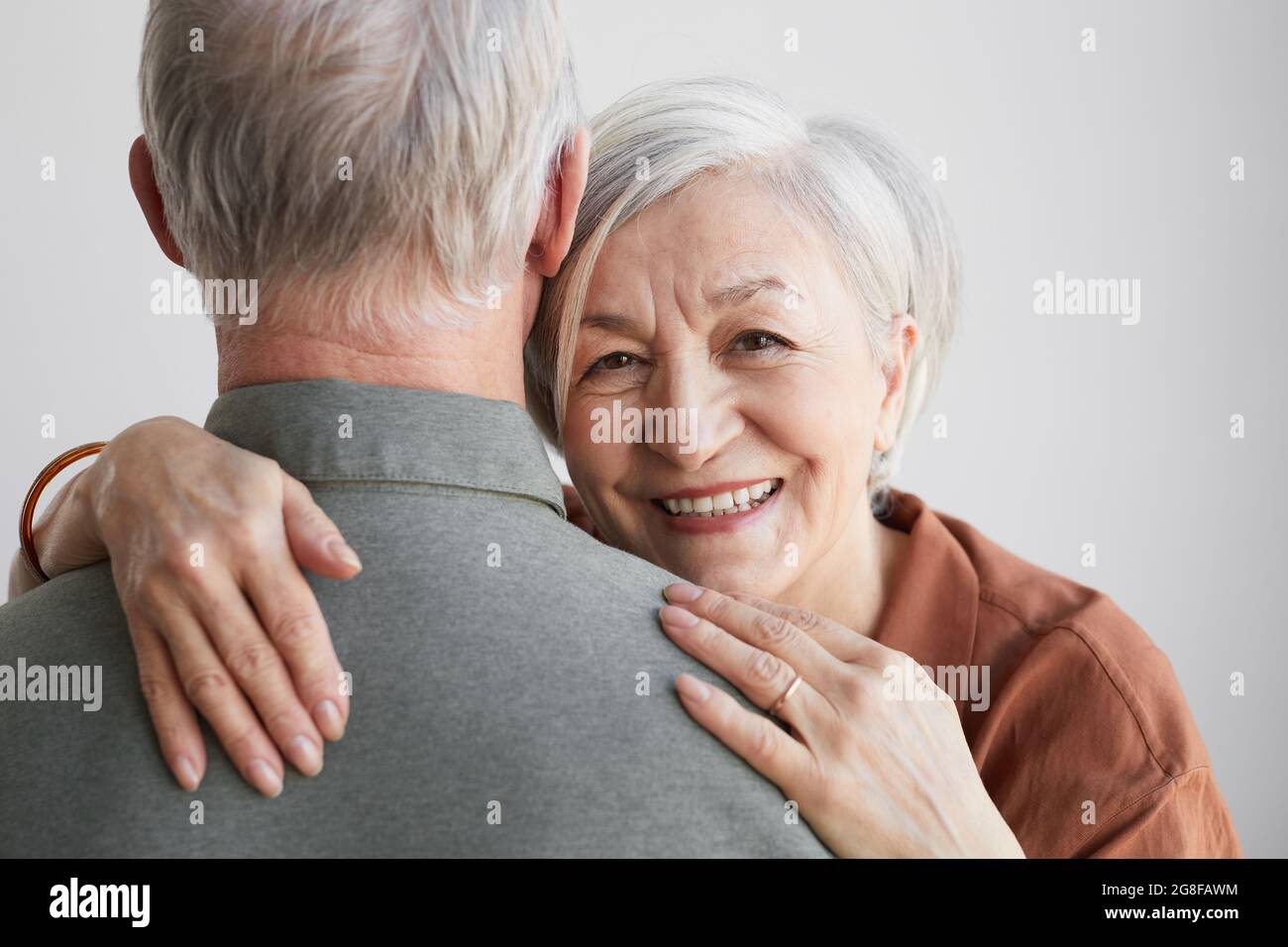 Portrait d'une femme âgée heureuse, épousant son mari et regardant l'appareil photo sur fond blanc Banque D'Images
