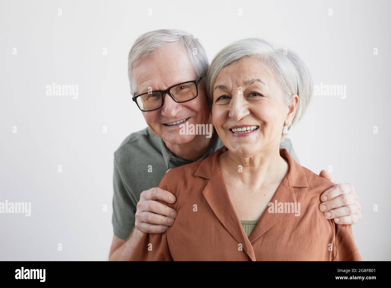 Portrait minimal d'un couple senior heureux qui embrasse son mari et regarde l'appareil photo sur fond blanc Banque D'Images