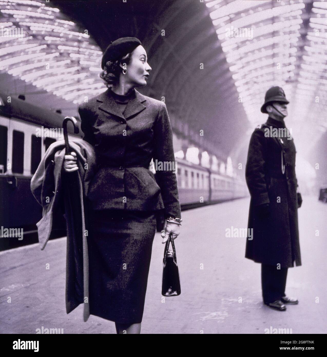 Toni Frissell photo de la mannequin de mode Lisa Fonssagrives qui se glissera par-dessus son épaule jusqu'à l'emblématique bobby de Londres.Probablement la gare de Paddington. Banque D'Images