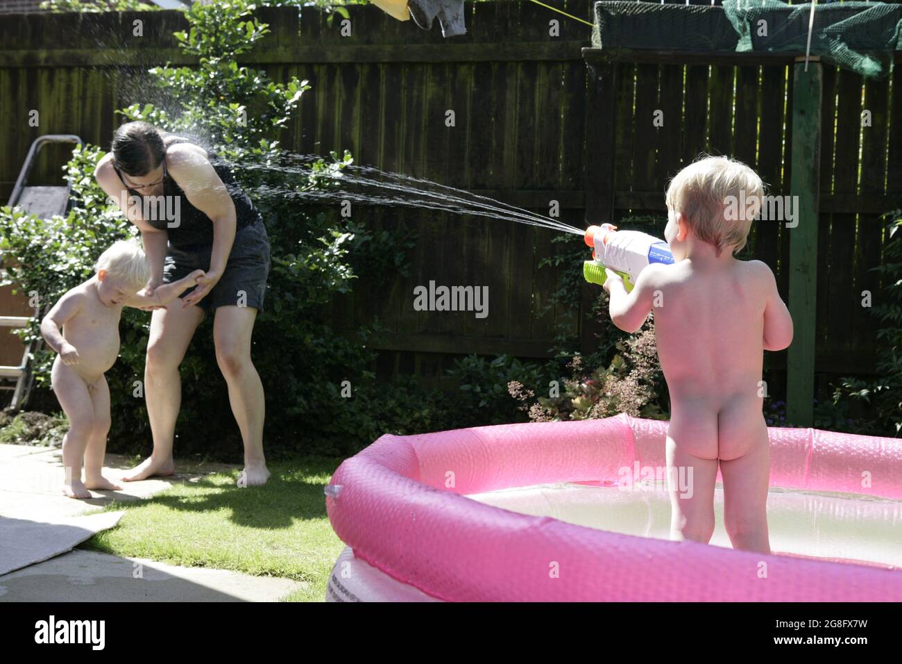 Frères nus, jeunes enfants de sexe masculin s'éclabousser et jouer avec leur mère dans la pataugeoire dans le jardin pendant la vague de chaleur estivale anglaise, juillet 2021 Banque D'Images