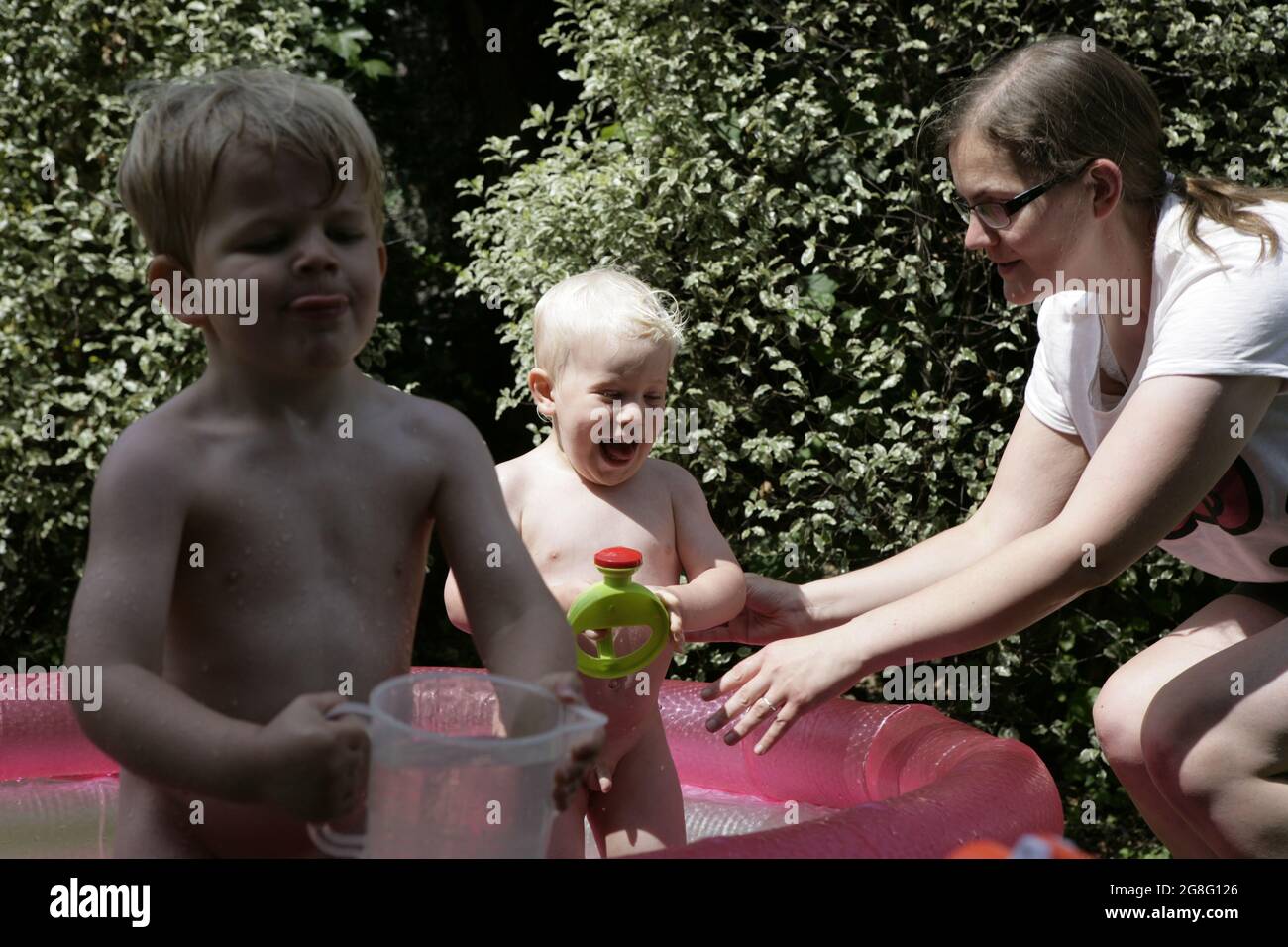 Frères nus, jeunes enfants de sexe masculin s'éclabousser et jouer avec leur mère dans la pataugeoire dans le jardin pendant la vague de chaleur estivale anglaise, juillet 2021 Banque D'Images