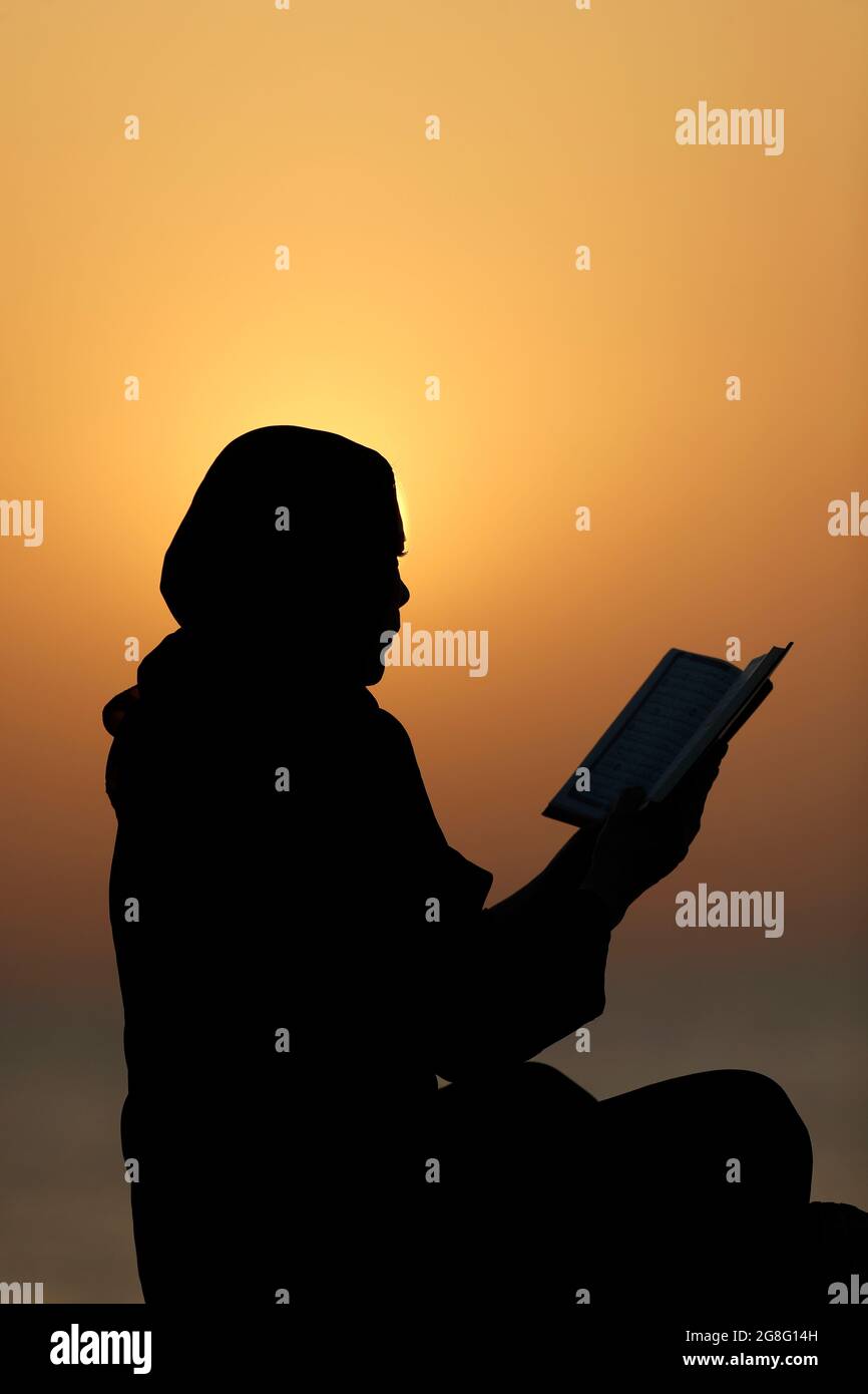 Silhouette d'une femme musulmane lisant le Noble Coran au coucher du soleil, Émirats arabes Unis, Moyen-Orient Banque D'Images