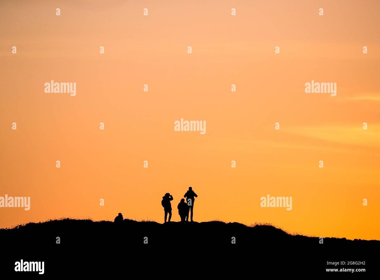 Les gens regardent le coucher du soleil sur le sommet de la montagne Cavehill, surplombant Belfast en Irlande du Nord, le plus long jour de l'année pendant le solstice d'été. Banque D'Images