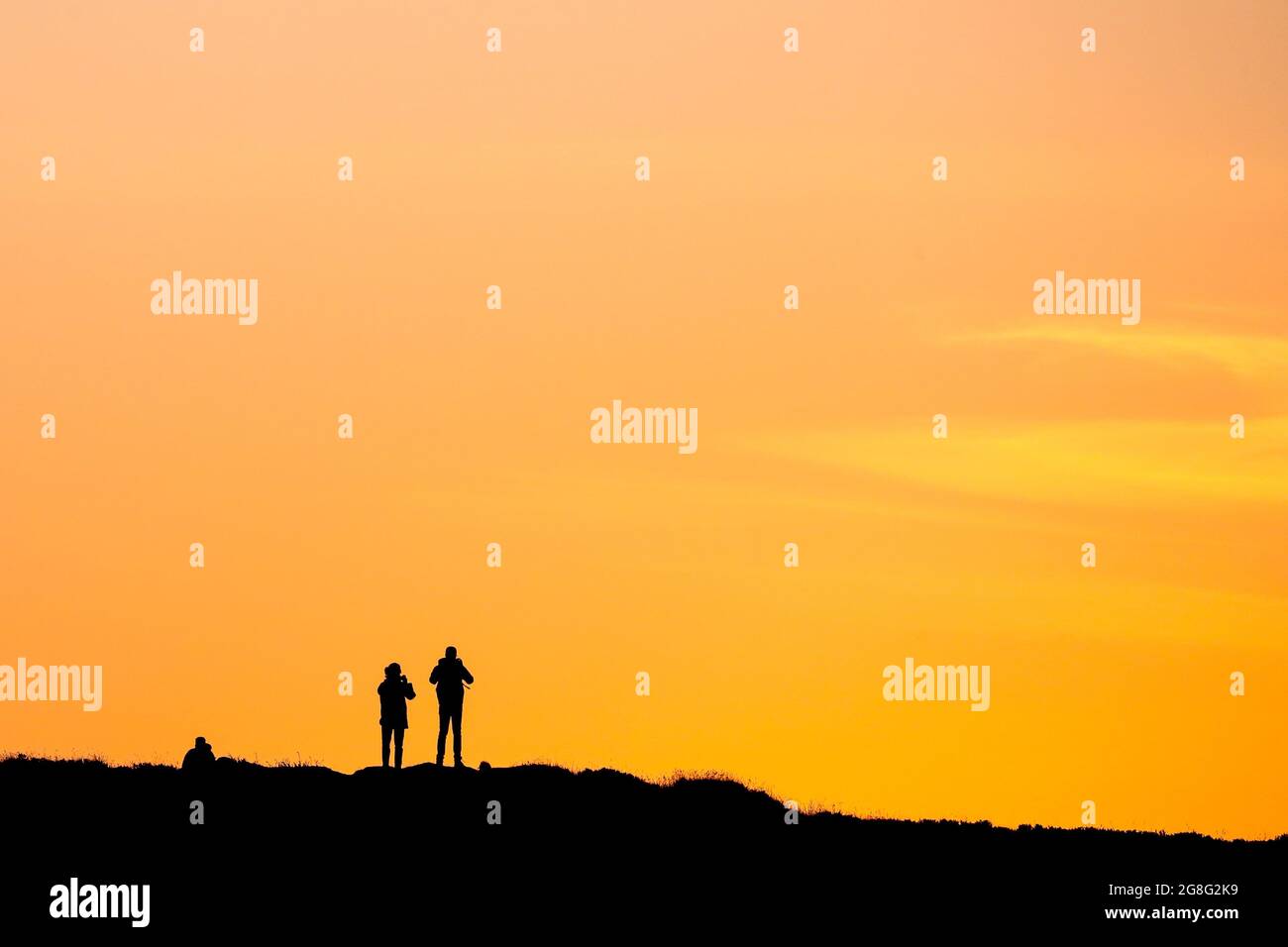 Les gens regardent le coucher du soleil sur le sommet de la montagne Cavehill, surplombant Belfast en Irlande du Nord, le plus long jour de l'année pendant le solstice d'été. Banque D'Images
