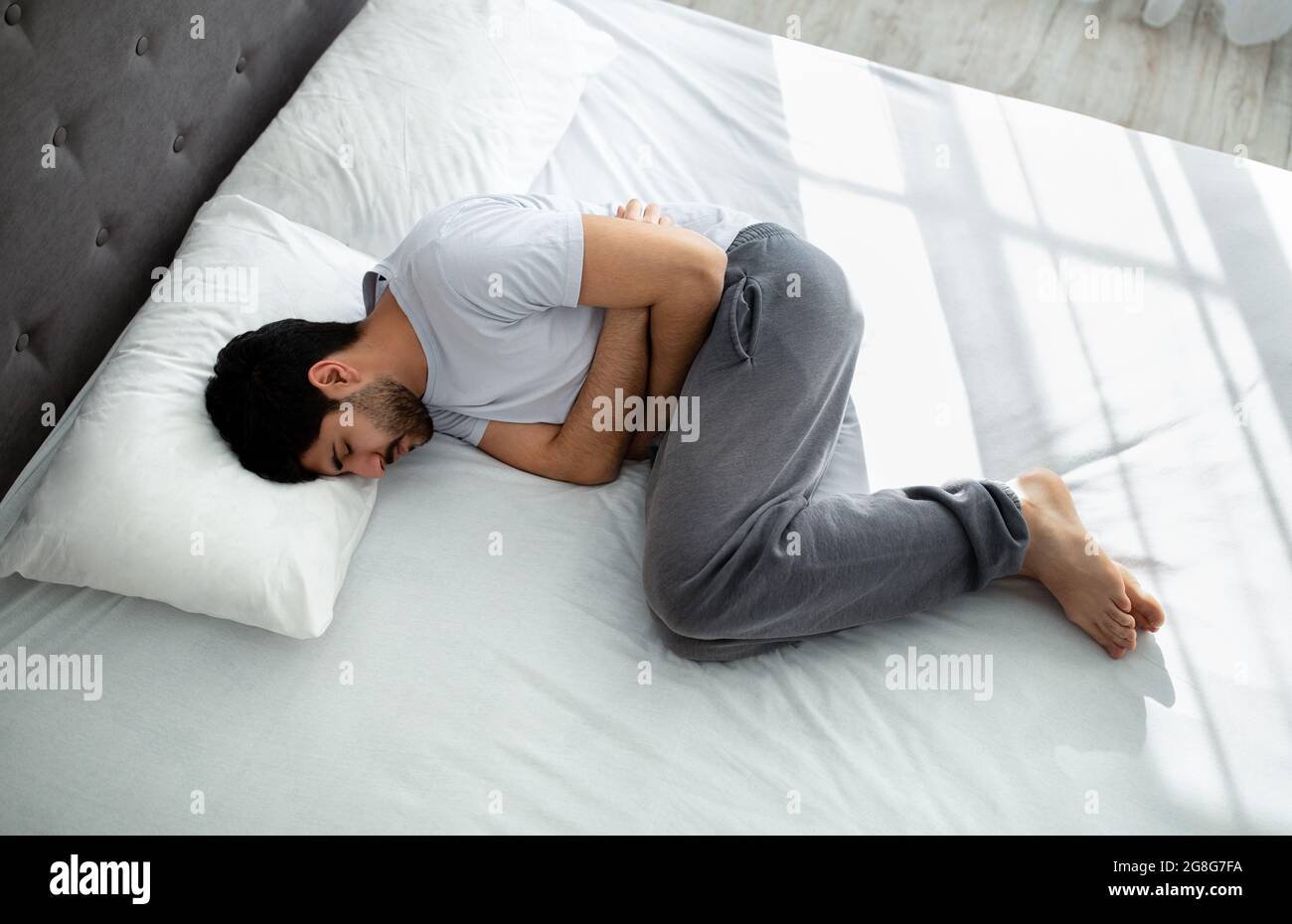 Stomachache. Jeune arabe mec souffrant de douleurs abdominales touchant l'estomac douloureux en étant allongé dans le lit, au-dessus de la vue Banque D'Images