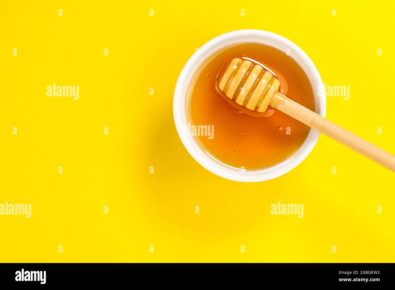 Miel dans un bol avec un balancier de miel sur fond jaune dans la vue de dessus plat, plan d'affichage, concept graphique, espace de copie Banque D'Images