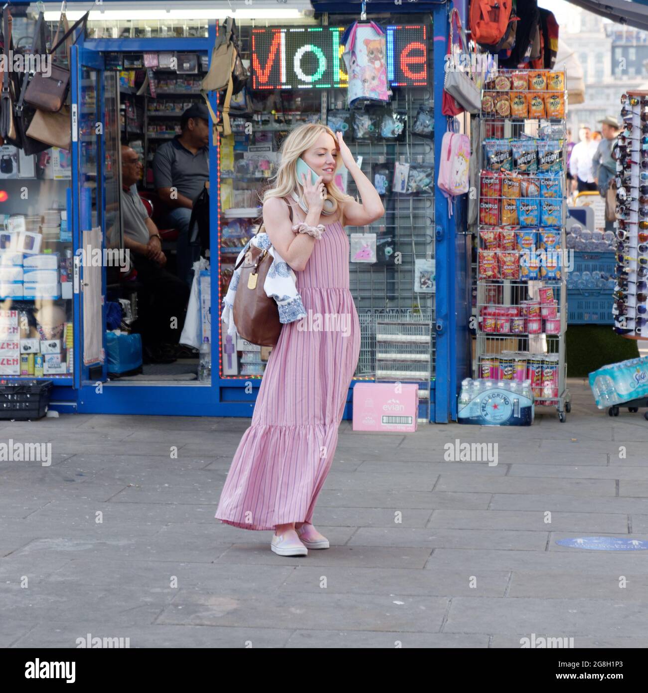 Londres, Grand Londres, Angleterre, 12 juin 2021 : jeunes femmes vêlées d'une robe rose avec un sac à main marron au téléphone devant un magasin bleu. Banque D'Images