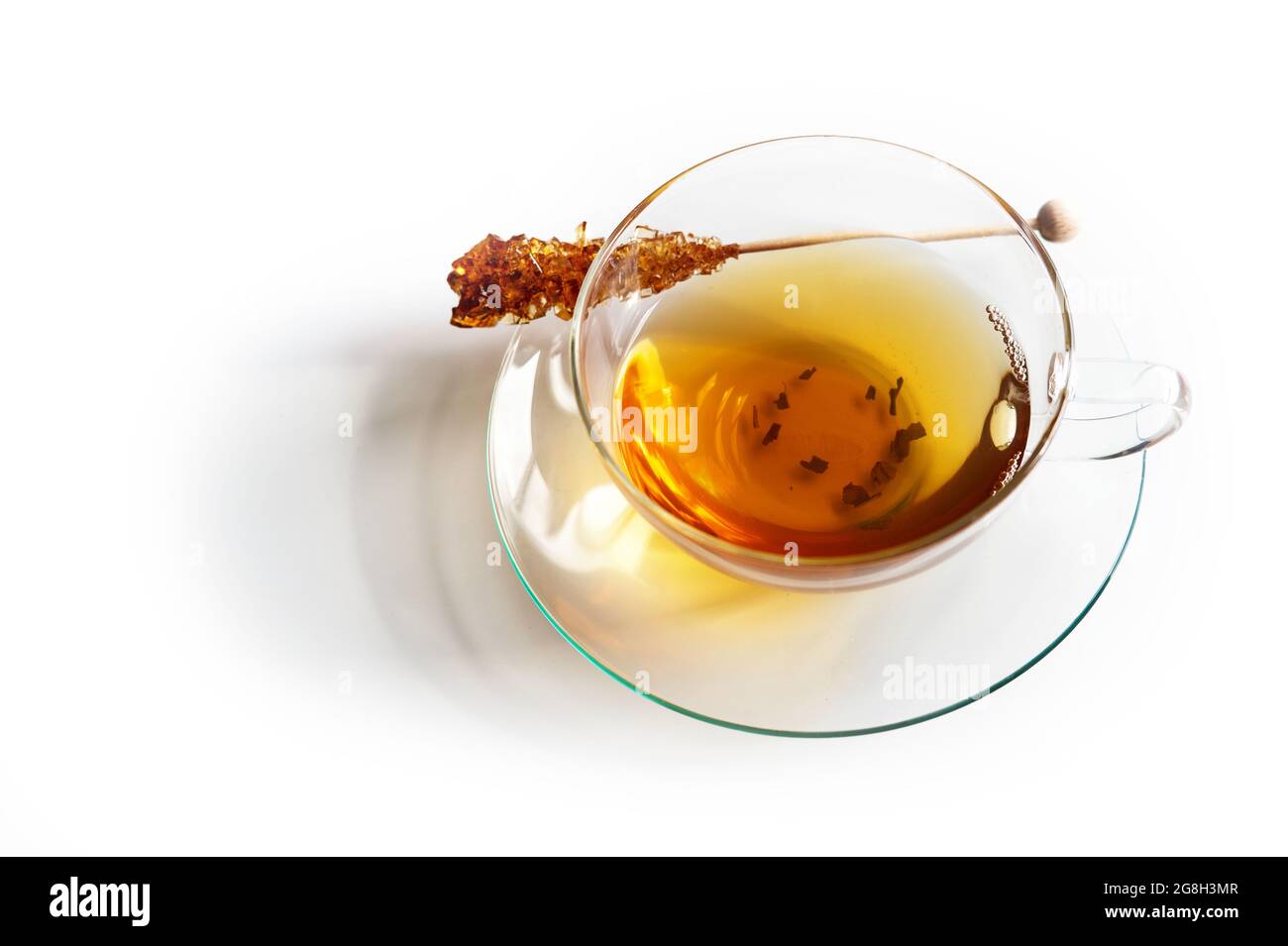 Tasse en verre à moitié remplie de thé noir et un bâton de sucre d'orge avec ombre réfléchissante sur un fond blanc, espace de copie, mise au point sélectionnée, profondeur étroite de Banque D'Images