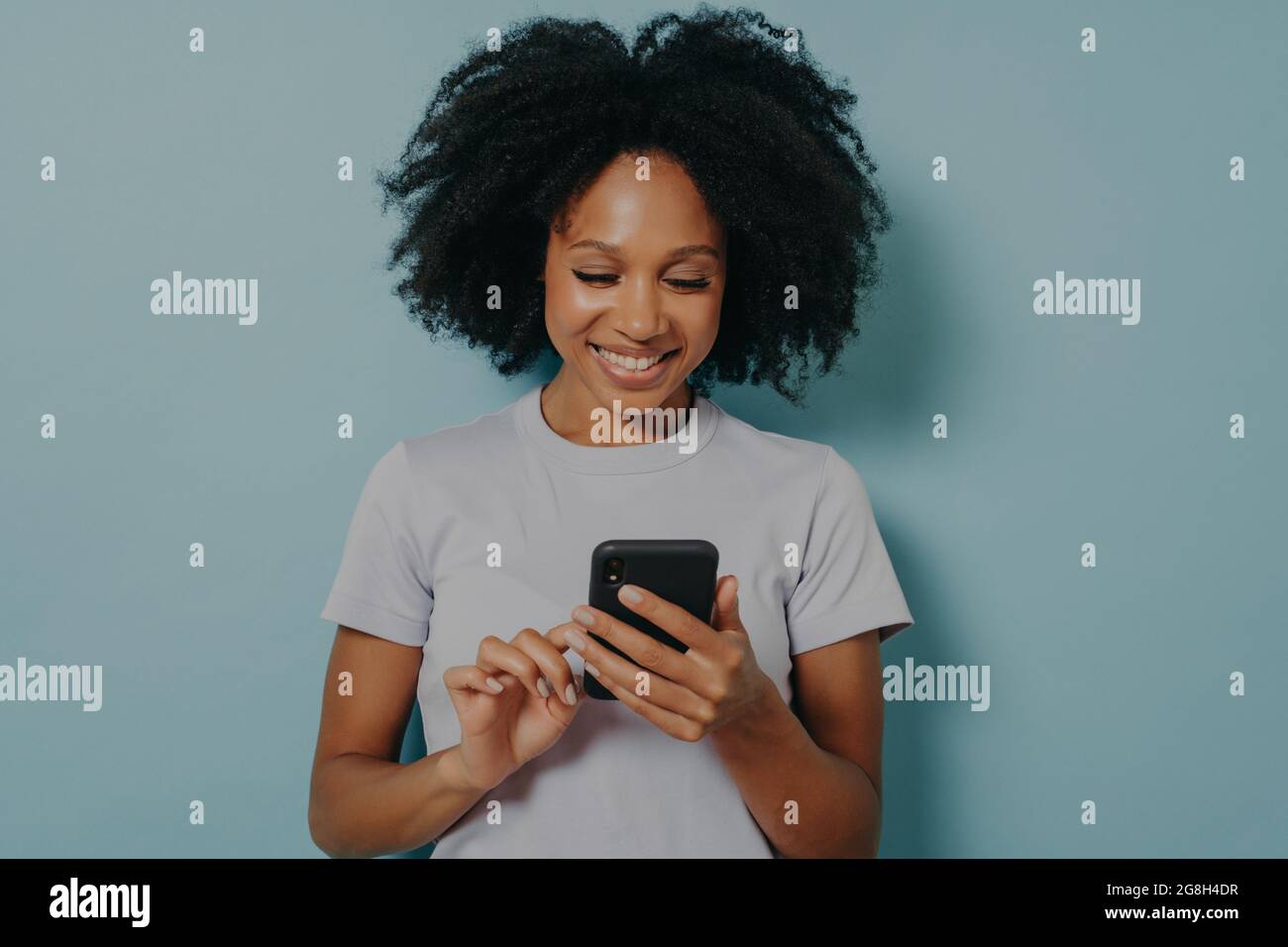 Jolie femme de cheveux bouclés tient le téléphone mobile moderne, saisit des messages sur un appareil de smartphone Banque D'Images