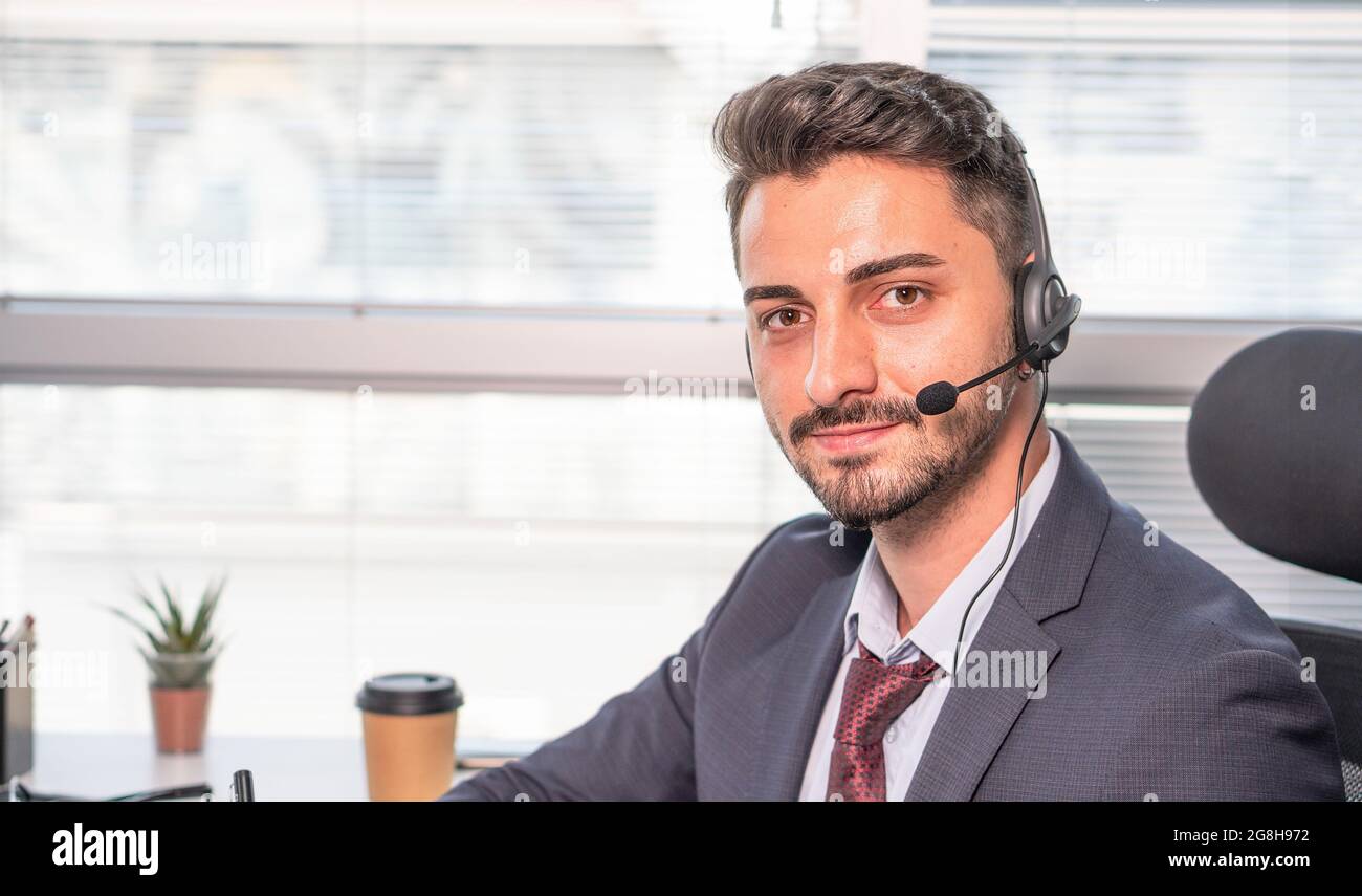 Portrait d'homme d'affaires, agent de centre d'appels portant un micro-casque travaillant avec un ordinateur portable au bureau. Homme en costume consultant le client au téléphone dans la coutume Banque D'Images