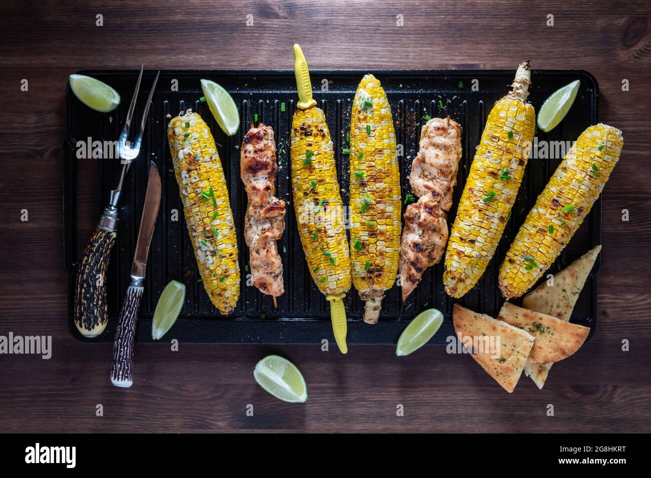 Vue de dessus en bas du maïs grillé sur la rafle avec des brochettes de poulet sur une poêle en fonte. Banque D'Images