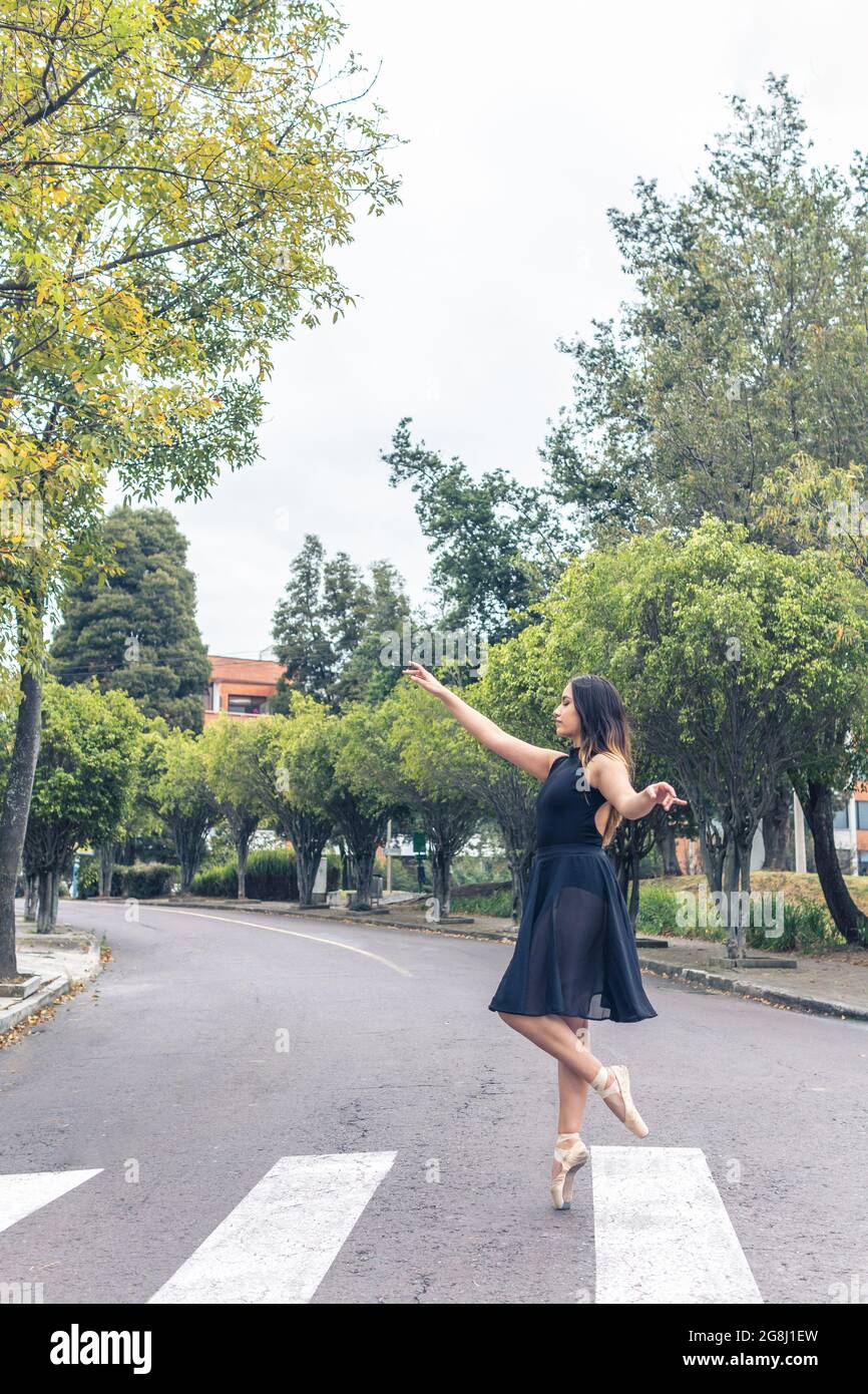 Photo verticale de la danseuse de ballet latine marchant avec élégance sur un pied à terre sur une passerelle piétonne avec une tenue noire et des chaussures pointe Banque D'Images