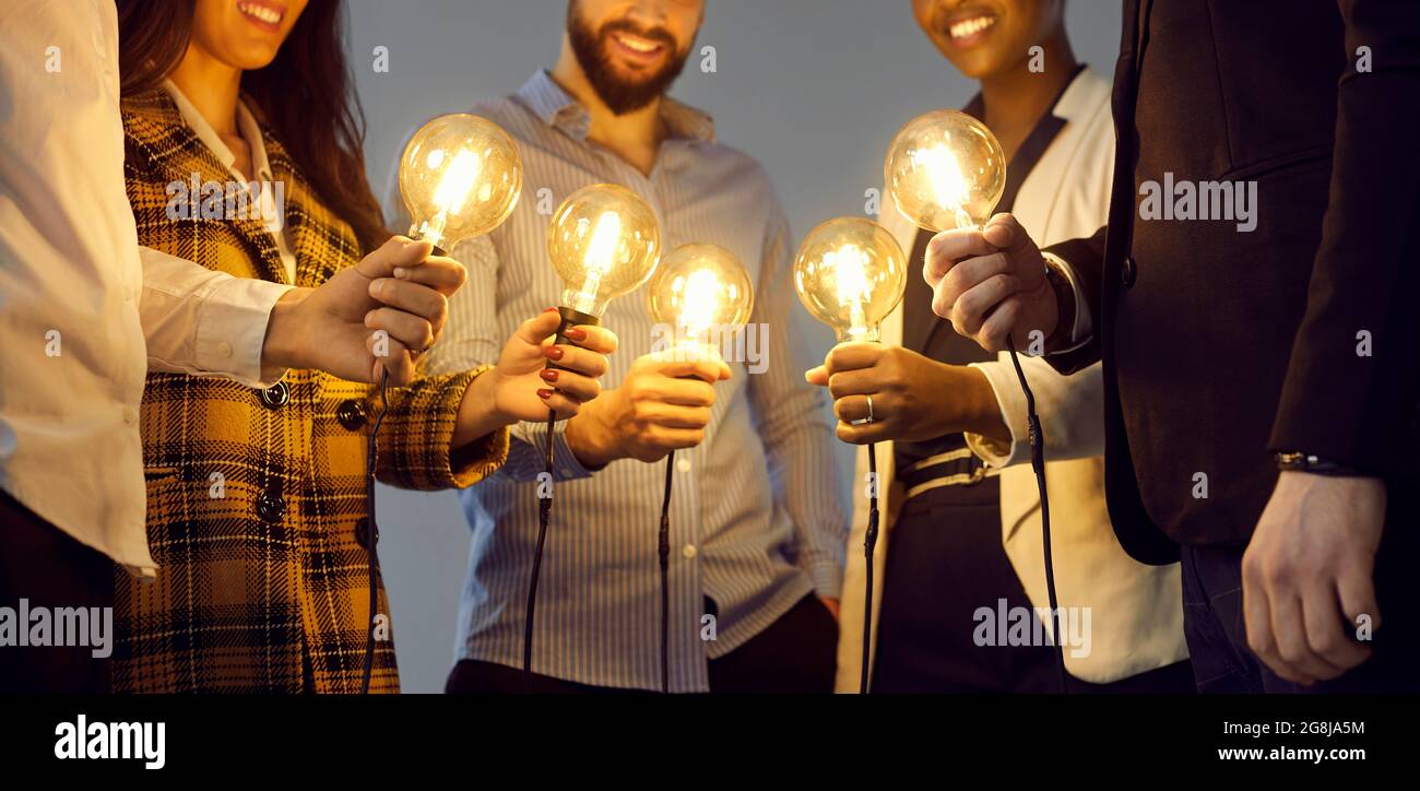 Des gens d'affaires heureux tenant des ampoules comme métaphore pour partager des idées dans la communauté créative Banque D'Images