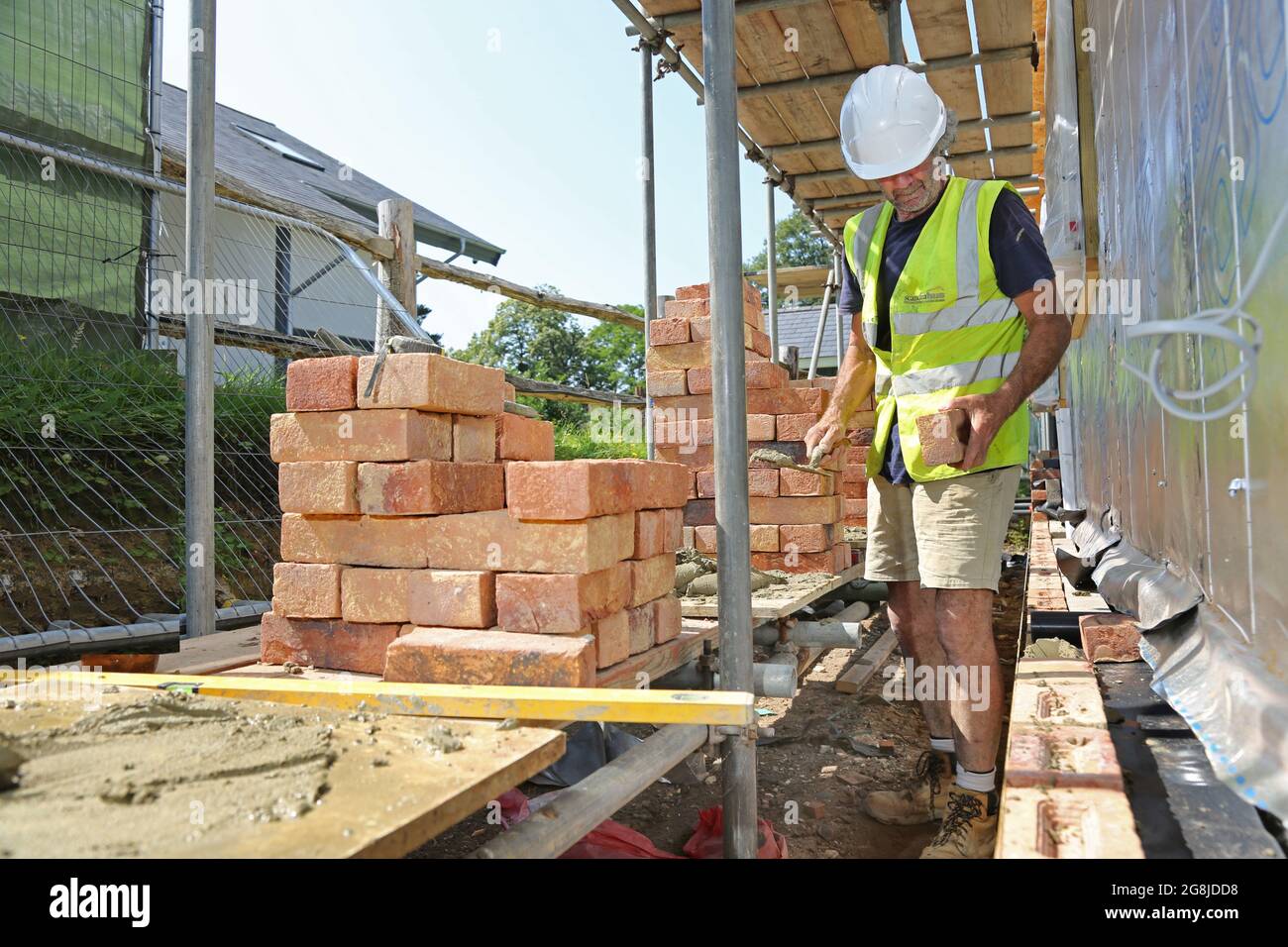 Une couche de brique construit le mur extérieur d'un nouveau bungalow à Surrey, au Royaume-Uni. Montre un échafaudage chargé de briques d'argile traditionnelles. Banque D'Images