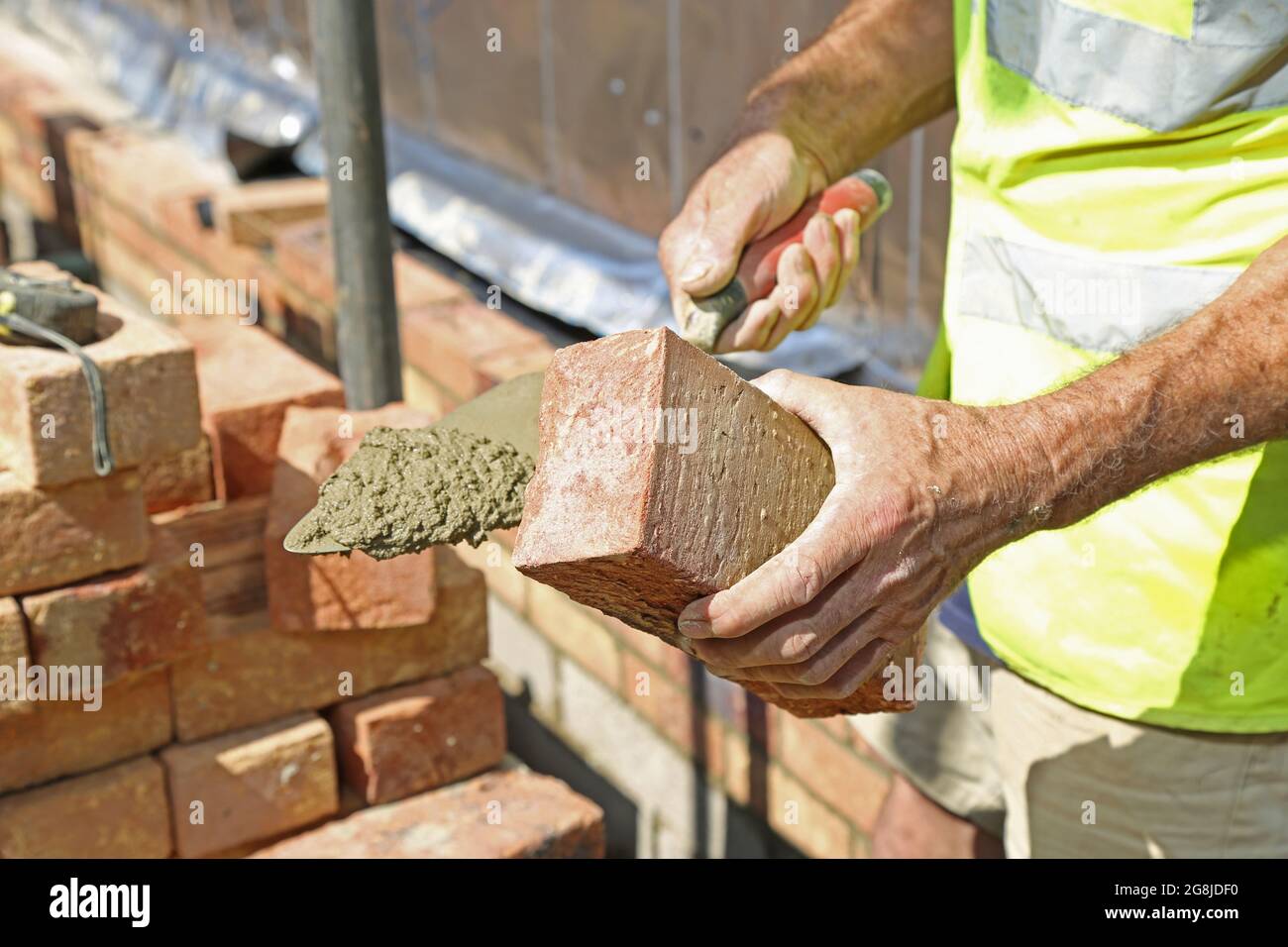 Gros plan d'une couche de briques construisant le mur extérieur d'un nouveau bungalow à Surrey, Royaume-Uni. Montre « beurrer » l'extrémité de la brique avec du mortier avant de poser. Banque D'Images
