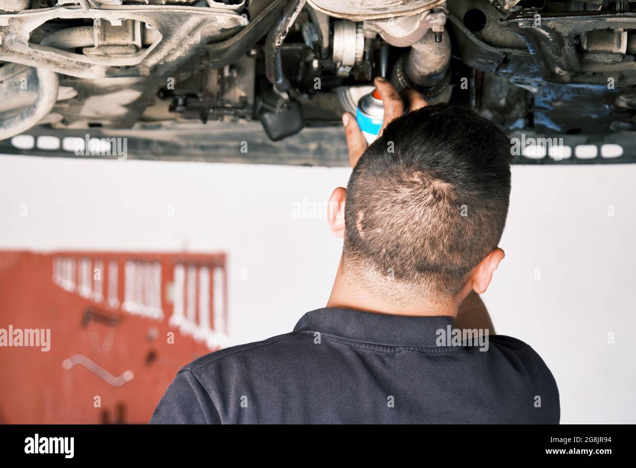 Mécanicien automobile utilisant un spray pour les parties inférieures d'une voiture soulevée à la station de réparation automatique. Banque D'Images