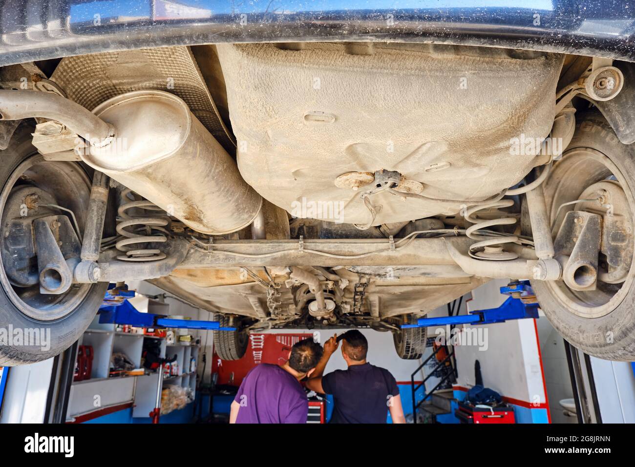 Deux mécaniciens vérifient une voiture soulevée au poste de réparation automobile. Banque D'Images