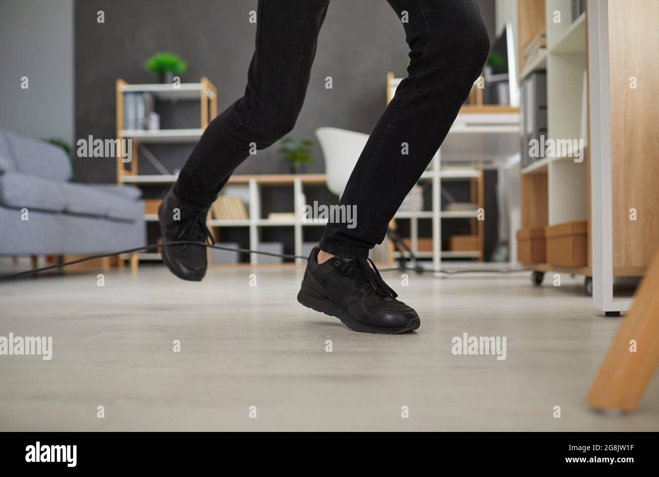 Gros plan sur les pieds d'un homme qui voyage au-dessus d'un cordon électrique à la maison ou au bureau Banque D'Images