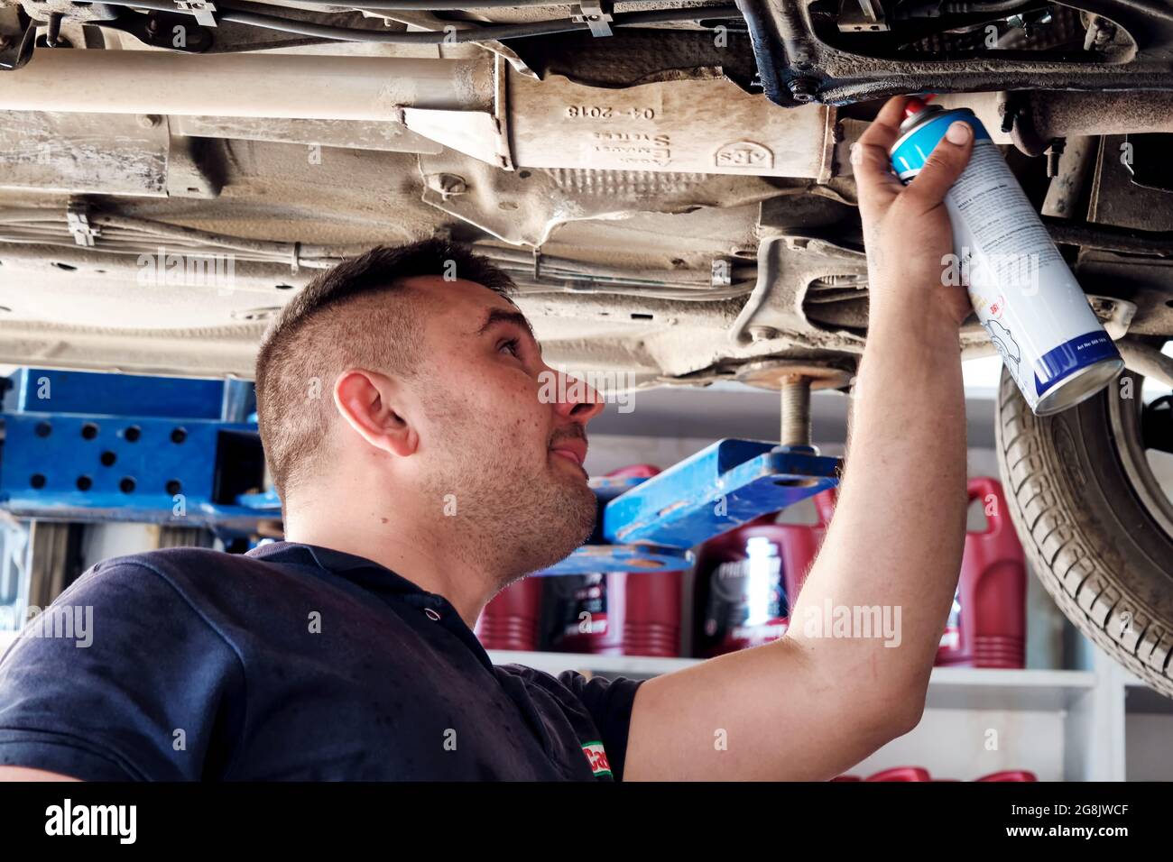 Urla, İzmir, Turquie - juin 2021 : mécanicien automobile utilisant un spray pour les parties inférieures d'une voiture soulevée à la station de réparation automobile. Banque D'Images