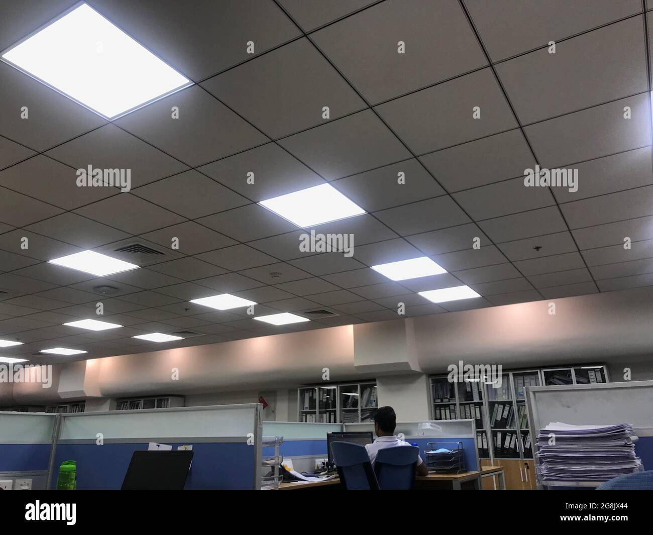 Un employé travaillant seul en raison d'une surcharge au bureau après les heures de travail dans un bureau qui est fini par le faux mobilier de plafond grille a Banque D'Images