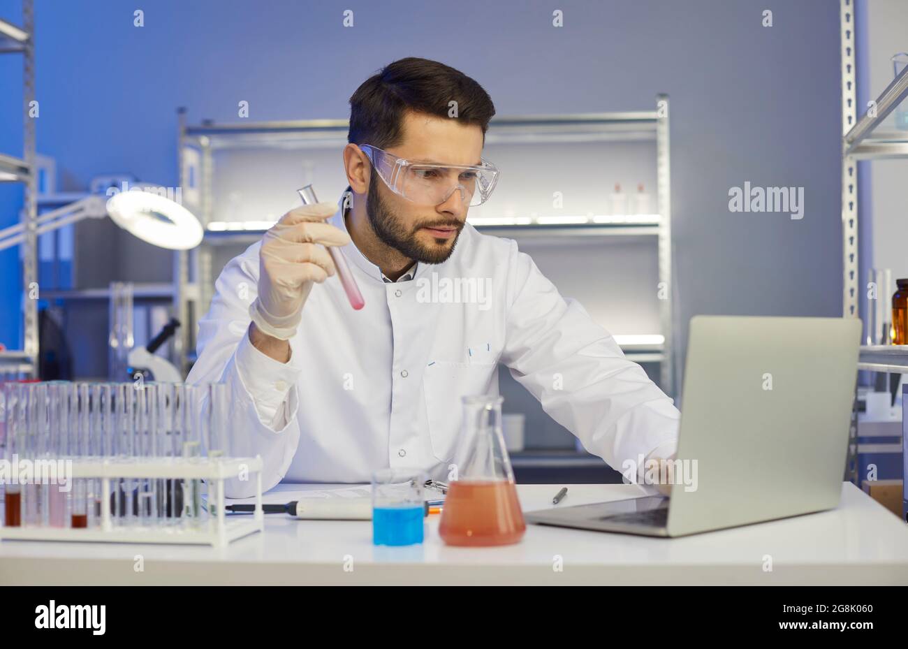 Homme scientifique avec tube à essai regardant le résultat de l'expérience de vérification de l'écran de l'ordinateur portable Banque D'Images