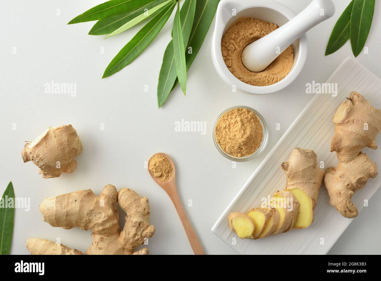 Poudre de gingembre préparée dans un pot de mortier et de verre et couper la racine sur la table blanche et les feuilles. Vue de dessus. Banque D'Images