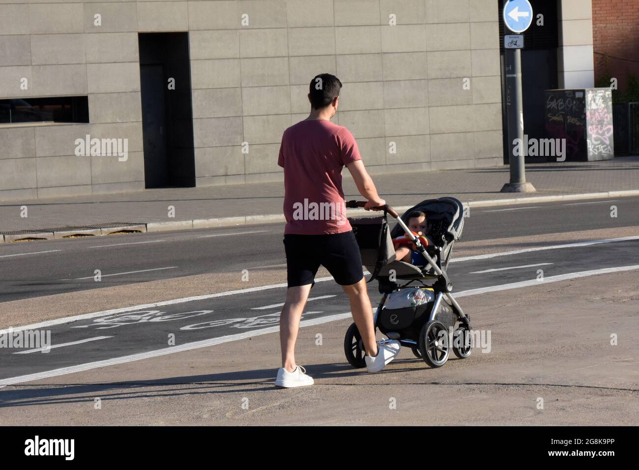 Vue arrière d'un père poussant une poussette avec son bébé à l'intérieur dans une rue en été. Banque D'Images