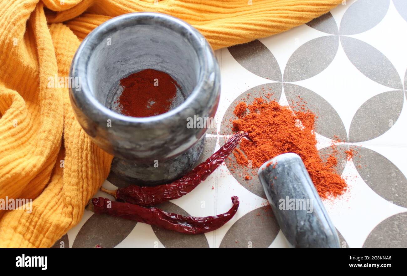 Mortier et pilon en pierre grise, piments et paprika en poudre sur une table. Photo vue du dessus des assaisonnements. Tissu jaune sur fond. Banque D'Images