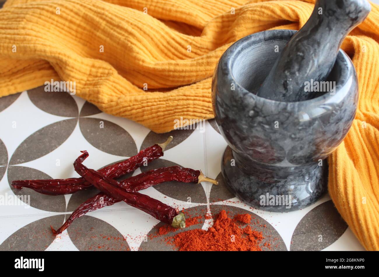 Mortier et pilon en pierre grise, piments et paprika en poudre sur une table. Photo vue du dessus des assaisonnements. Tissu jaune sur fond. Banque D'Images