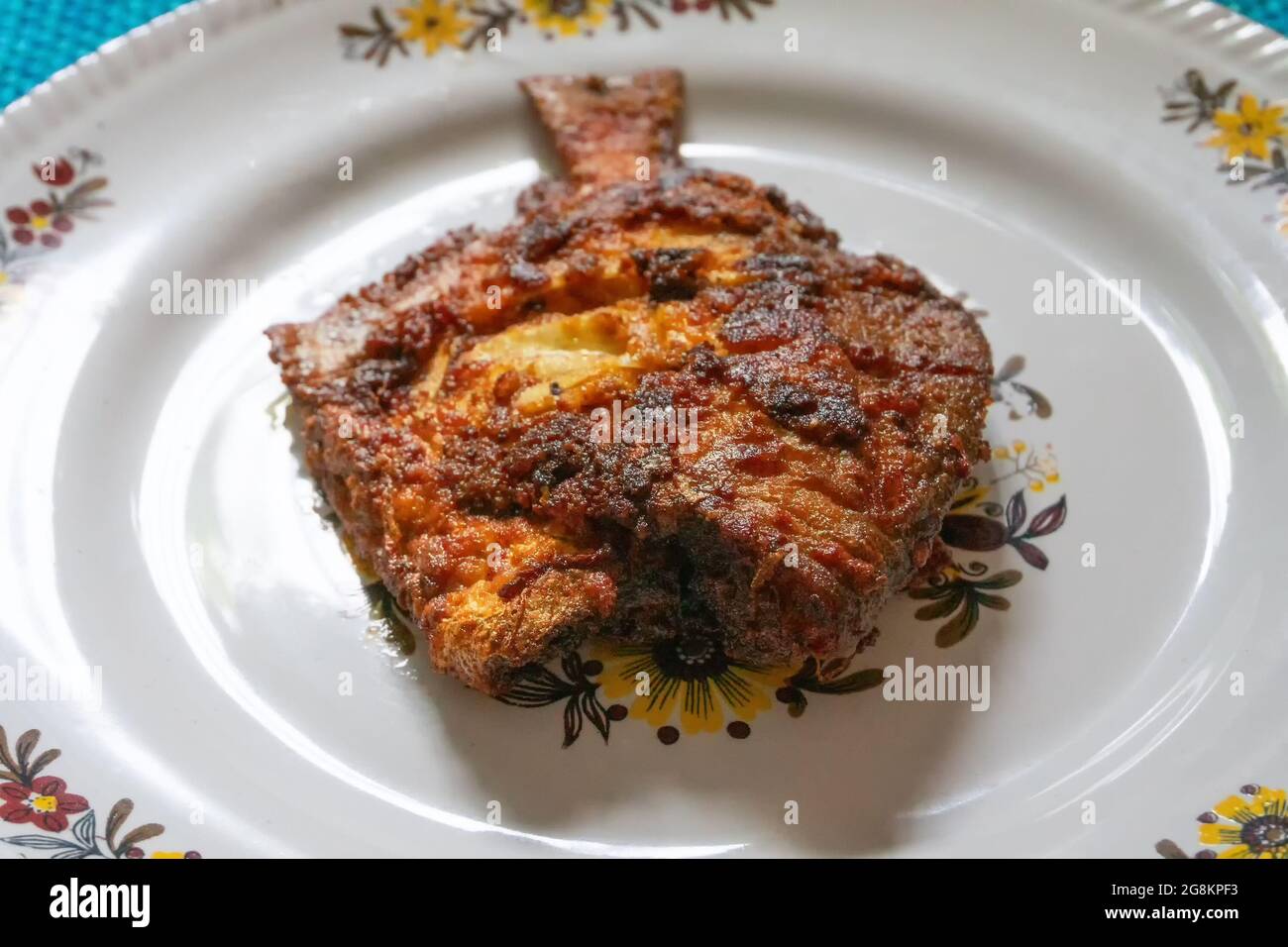 Un poisson frit servi sur un plateau blanc décoré, une cuisine indienne épicée. Les Pomfrets sont des poissons périformes appartenant à la famille des Bramidae. Banque D'Images