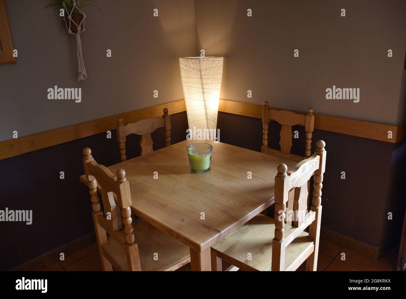 Table de restaurant au crépuscule avec lampe en papier allumée. Table, quatre chaises et bougie verte sur la table, lumière naturelle venant de la droite. Banque D'Images