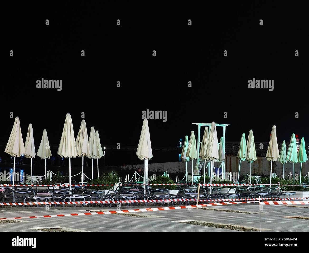 Plage de nuit vide avec chaises longues et parasols pliés clôturée avec ruban barrière Banque D'Images