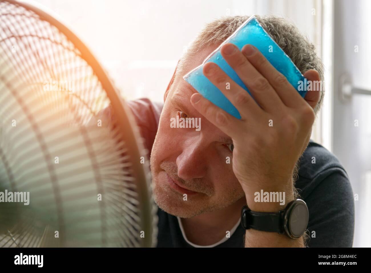 L'homme souffre de la chaleur et des maux de tête tout en étant assis dans  la chambre et essaie de se refroidir par le ventilateur Photo Stock - Alamy