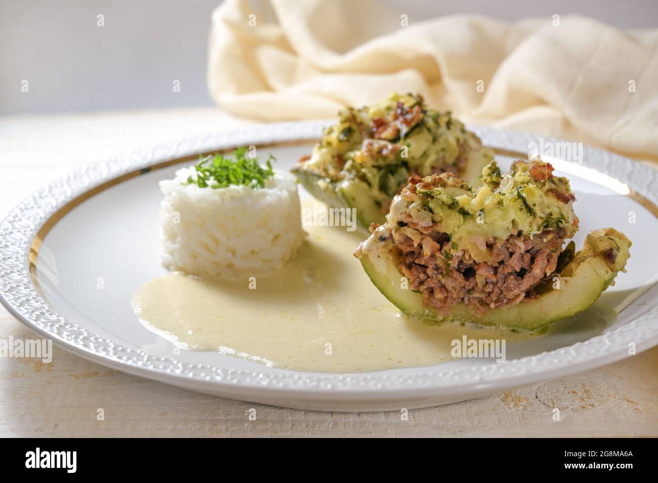 Courgette ou courgette cuite avec une garniture de bœuf haché, bacon et crème avec riz et sauce citron sur une assiette blanche, gros plan, mise au point sélectionnée Banque D'Images