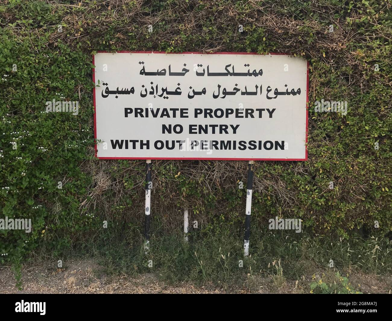 Tableau blanc de ''propriété privée pas d'entrée sans permission'' avec fond blanc sur une clôture verte et écrit en anglais et en arabe W Banque D'Images
