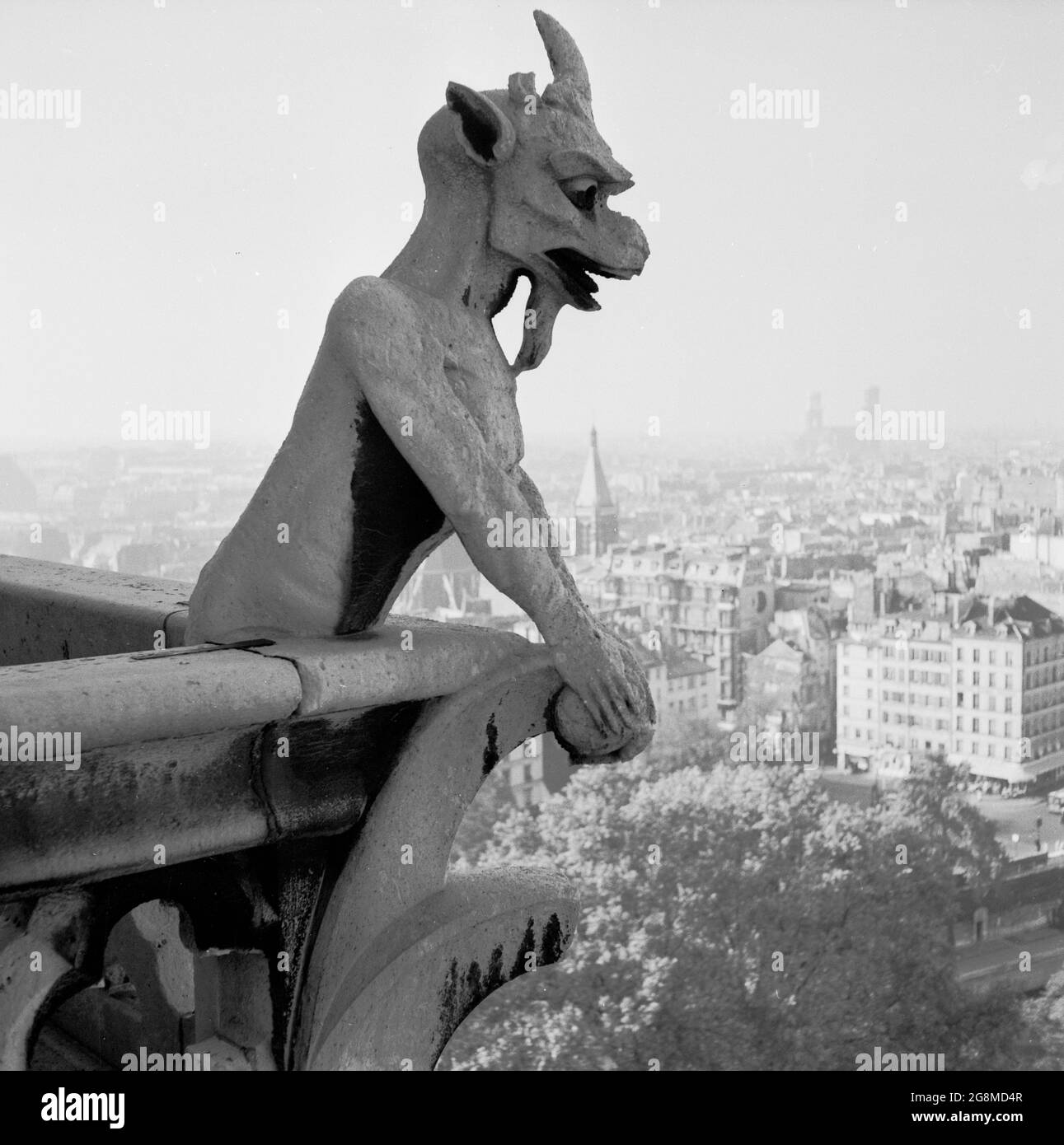 Années 1950, historique, la chimère de la cathédrale notre-Dame au-dessus de la ville de Paris, France. Contrairement aux célèbres gargouilles de notre-Dame, les figures de calcaire grotesques qui agissent comme des becs pour transmettre l'eau de pluie loin du toit, les statues de pierre de chimère ne dépassent pas des murs extérieurs. Au lieu de cela, ils bordent la Galerie des Chimères, un balcon qui relie les deux clochers. En se regardant au-dessus de la balustrade, où ils gardent le contrôle de la ville ci-dessous, ils ont été un nouvel ajout à la cathédrale au milieu des années 1800 lorsqu'elle a subi la restauration. Banque D'Images
