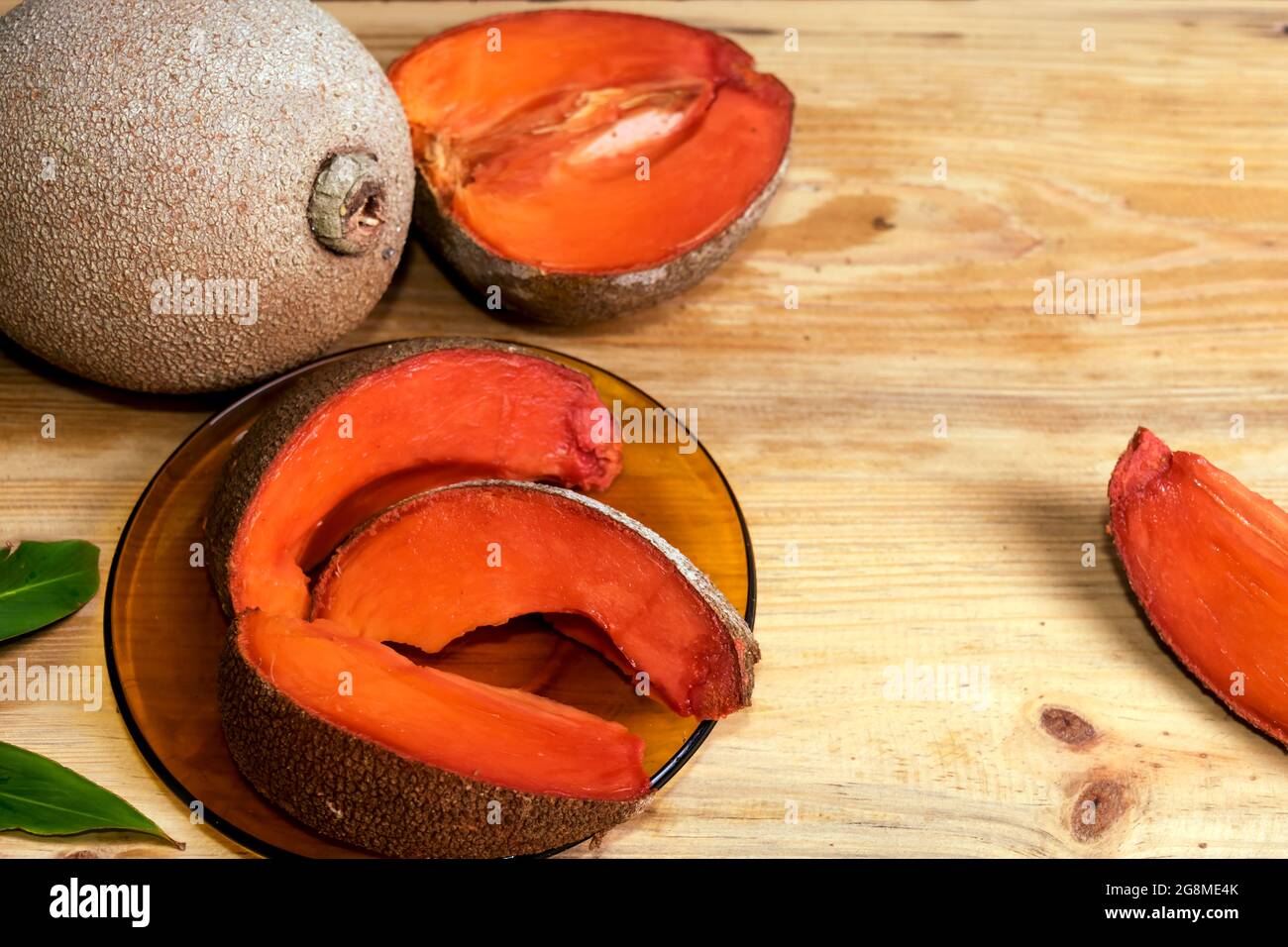 Tranches de prune sapodilla mûre sur un plat de cristal brun sur une table en bois, il y a aussi un fruit entier à proximité, et un demi coupé à côté Banque D'Images