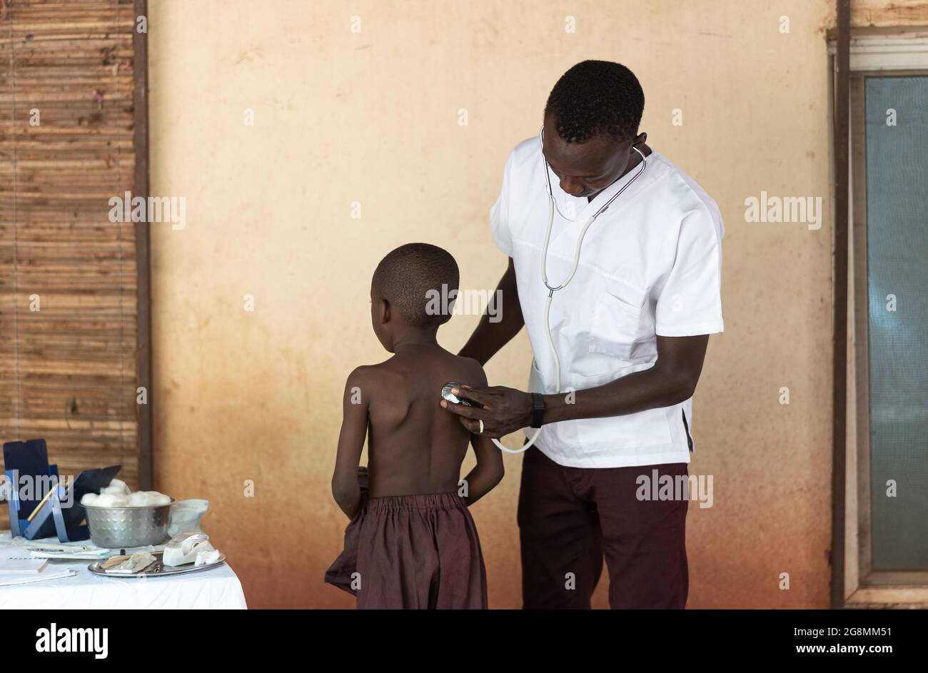 Une infirmière africaine porte un manteau de laboratoire à l'hôpital rural et inspecte et examine la santé d'un petit patient africain. Banque D'Images